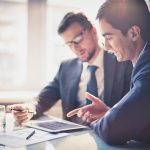 Image of two young businessmen using touchpad at meeting